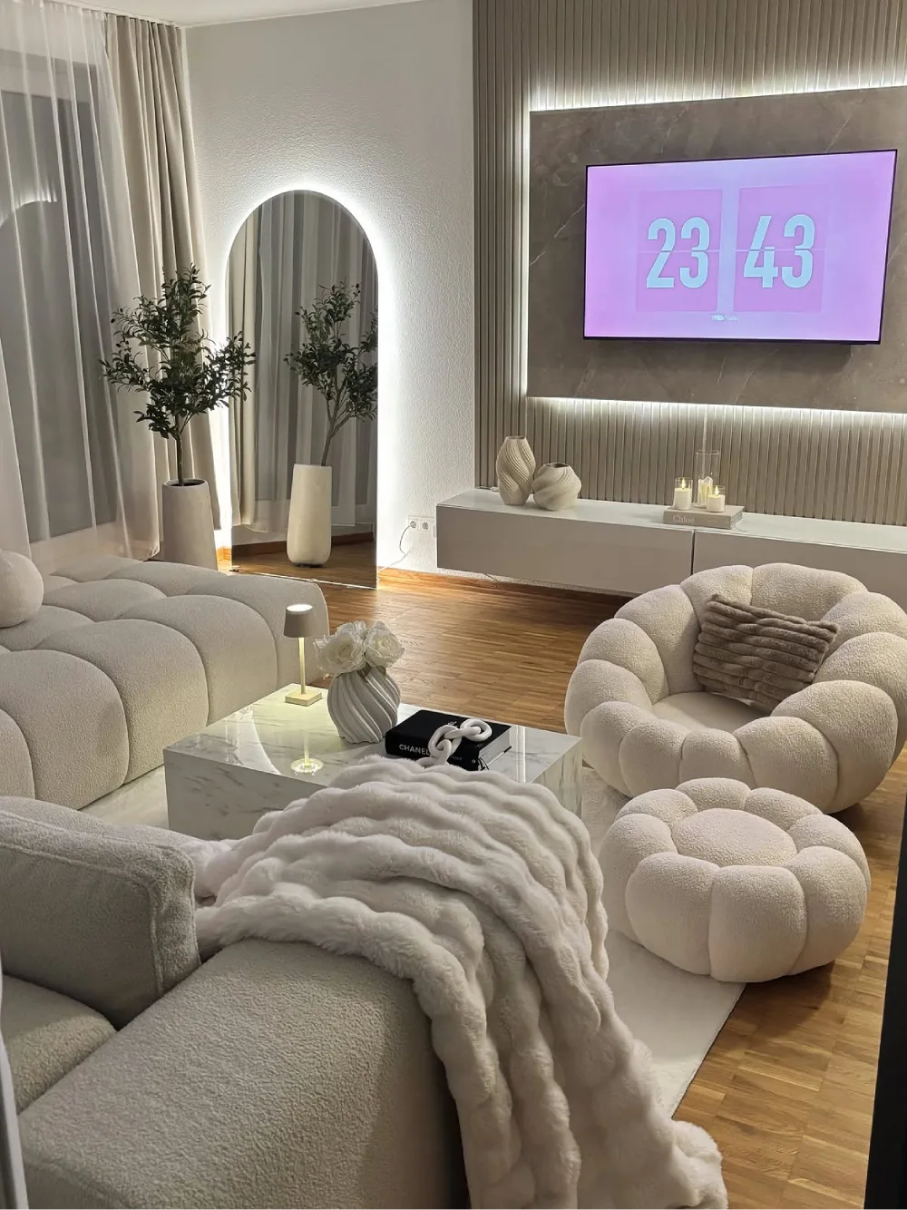 modern white living room with sculptural furniture, arched mirror, and wood flooring