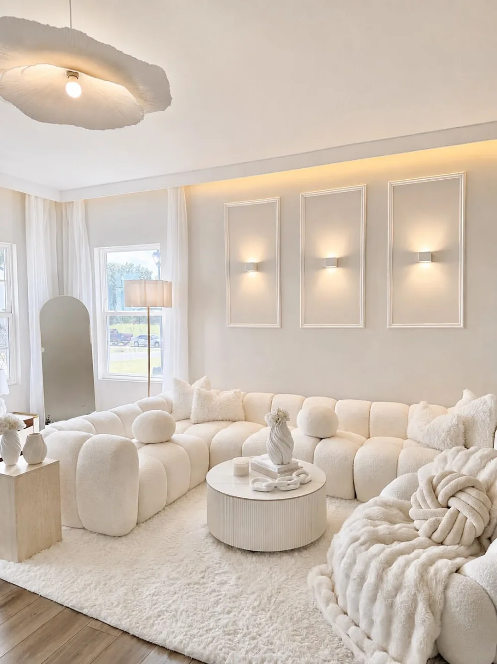 all-white living room with curved sectional sofa, textured rug, and soft wall lighting