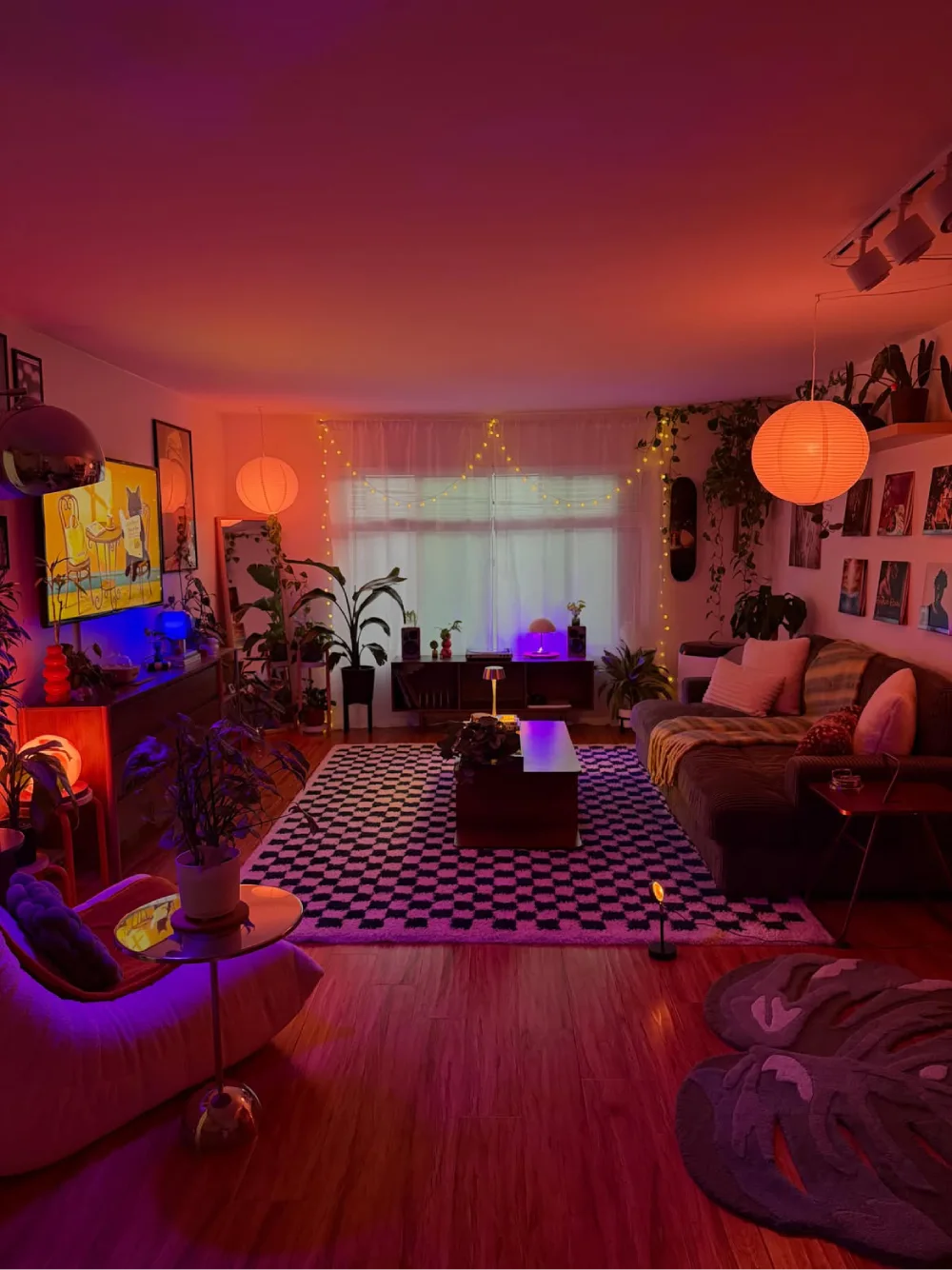 Colorful living room glowing with red and purple lighting, plants, artwork, and cozy seating