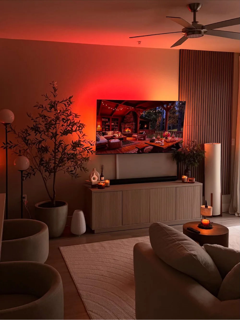 Modern living room with TV, warm red lighting, neutral sofas, and a cozy rug