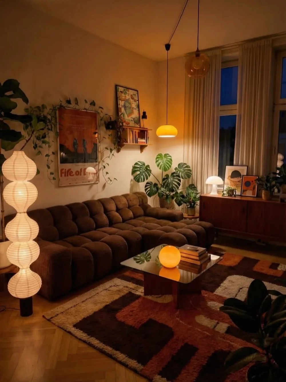Moody living room with deep brown sectional, plants, paper lamps, and warm ambient lighting