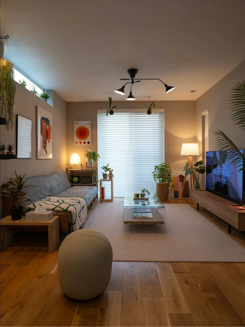 Warm apartment living room with a gray sofa, wood furniture, plants, and soft ambient lighting