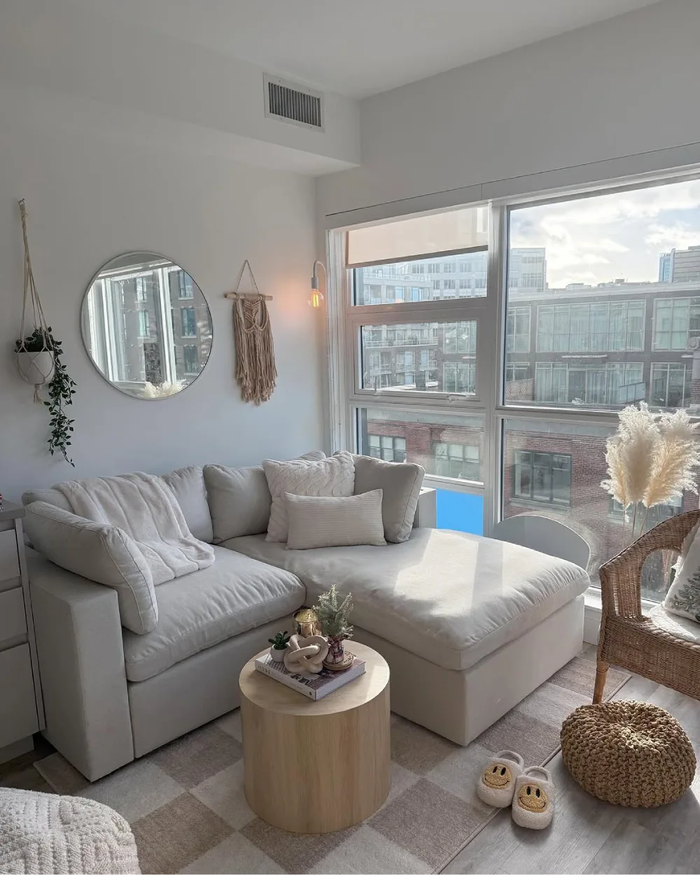 Bright apartment living room with a white sectional, round wood table, and large windows