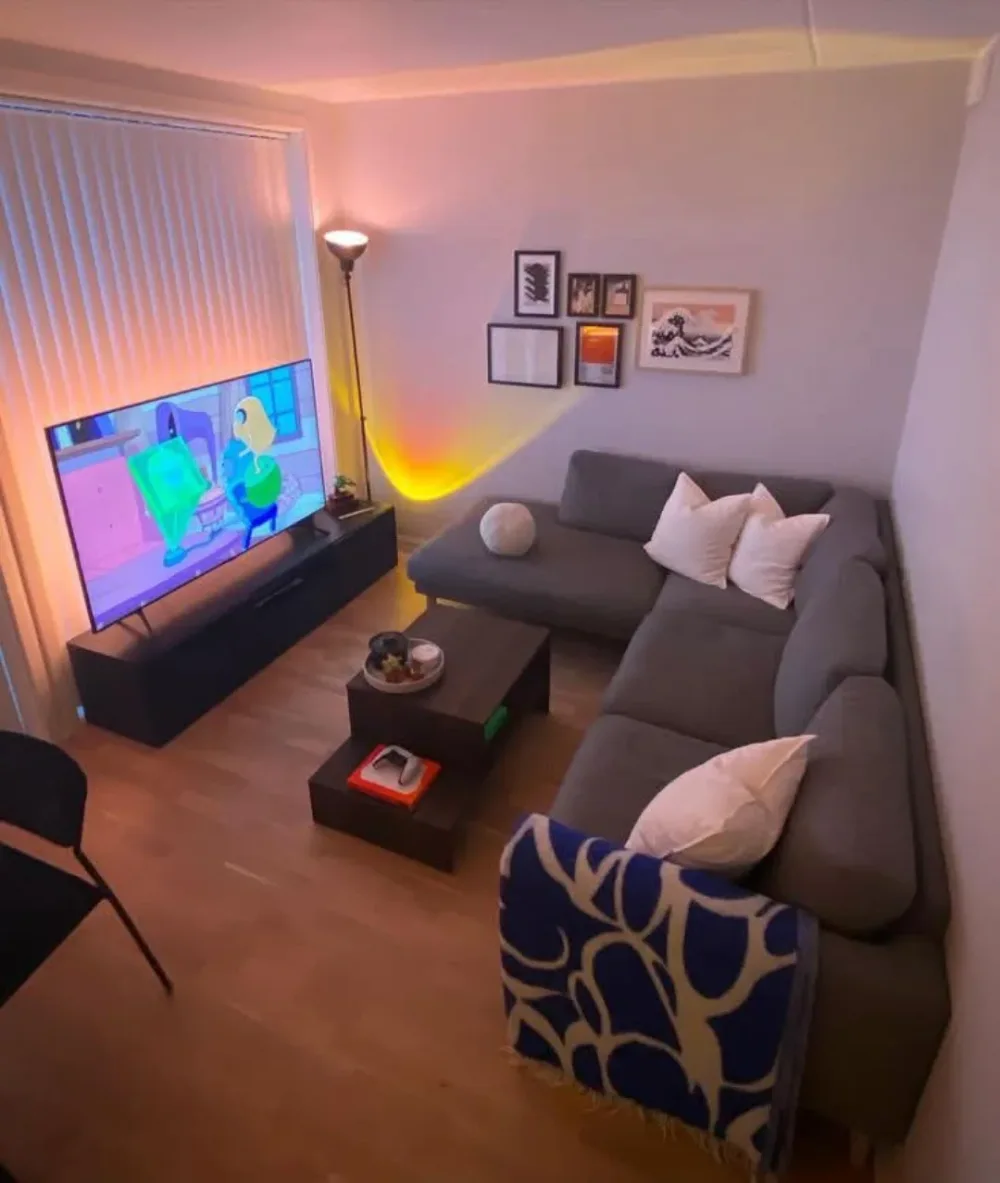 Cozy apartment living room with a gray sectional, television, warm accent lighting, and framed artwork