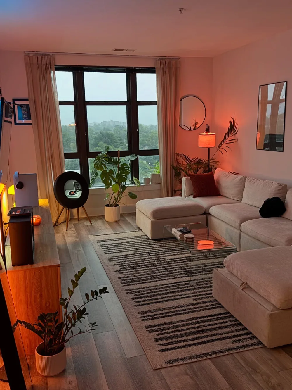 Cozy apartment living room with a cream sectional, plants, striped rug, and warm ambient lighting