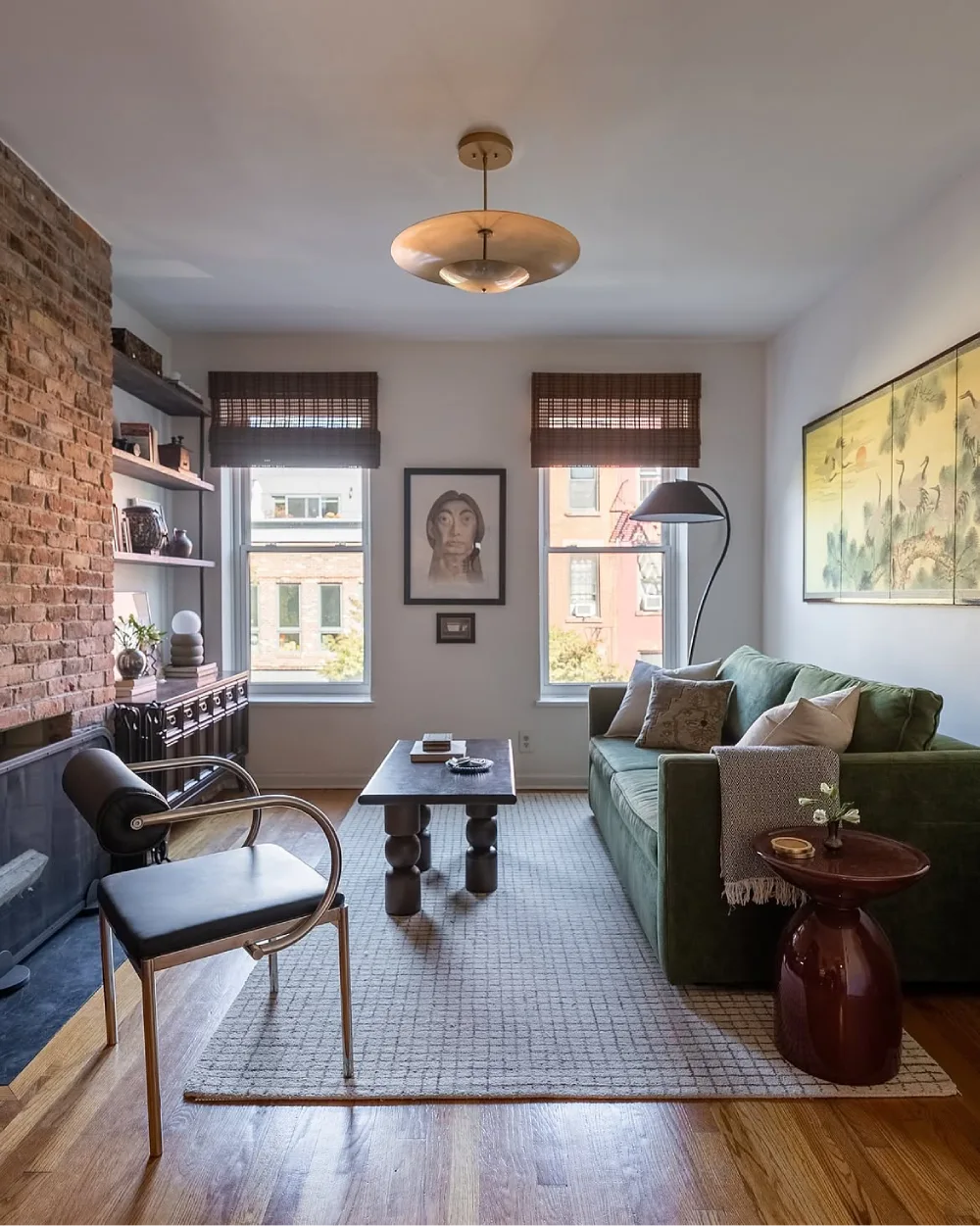 Apartment living room with a green sofa, exposed brick wall, wood furniture, and woven rug