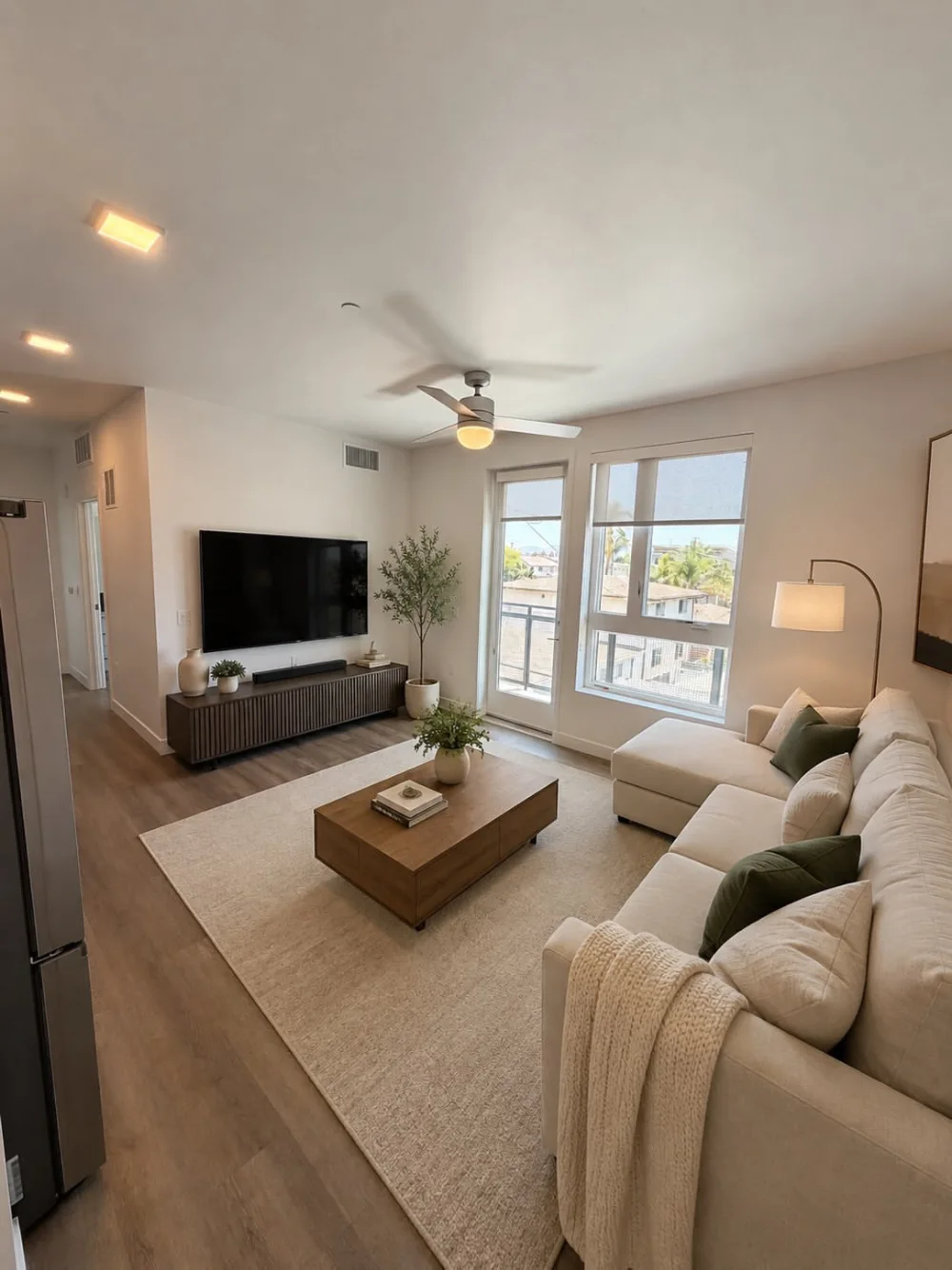 Apartment living room with a large cream sectional, wood coffee table, TV console, and balcony doors