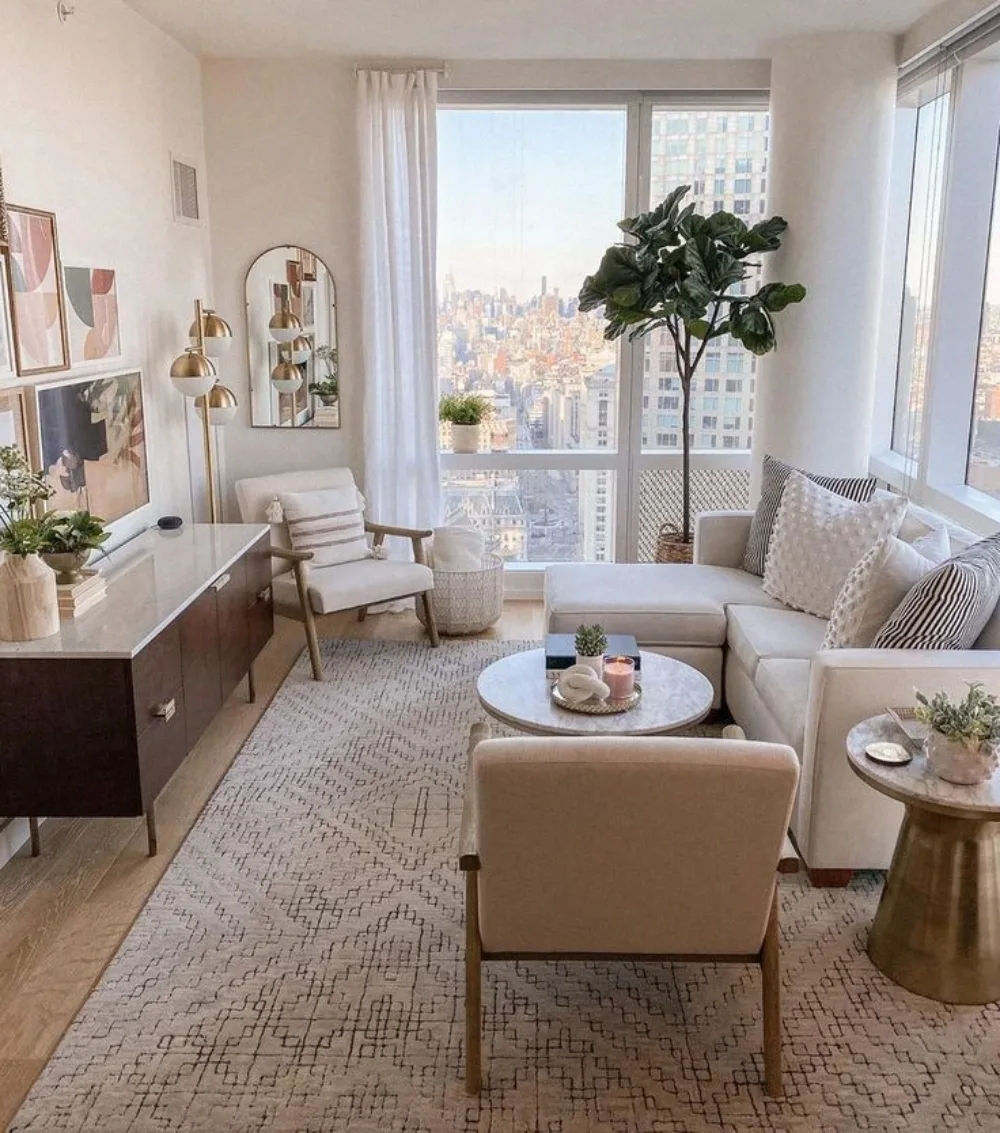 Neutral apartment living room with a cream sectional, patterned rug, wood furniture, and city views