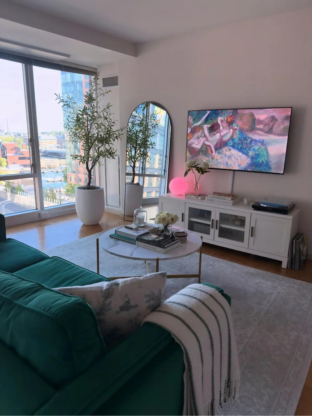 Apartment living room with a deep green sofa, large mirror, plants, and colorful artwork
