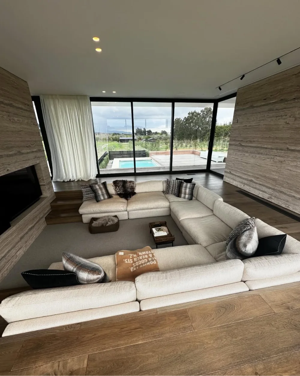 Sunken living room with a cream sectional and wide windows overlooking a pool