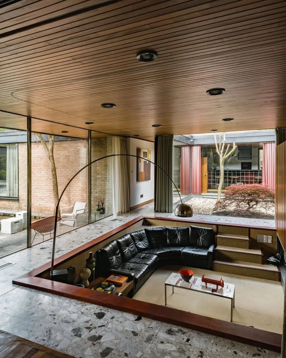 Midcentury sunken living room with black leather seating and wood ceiling