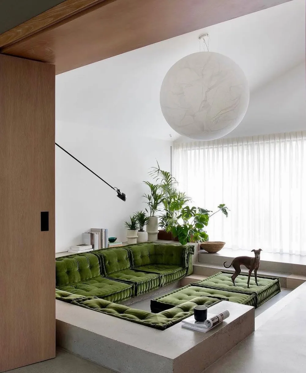 Sunken living room with green tufted seating and a large round pendant light