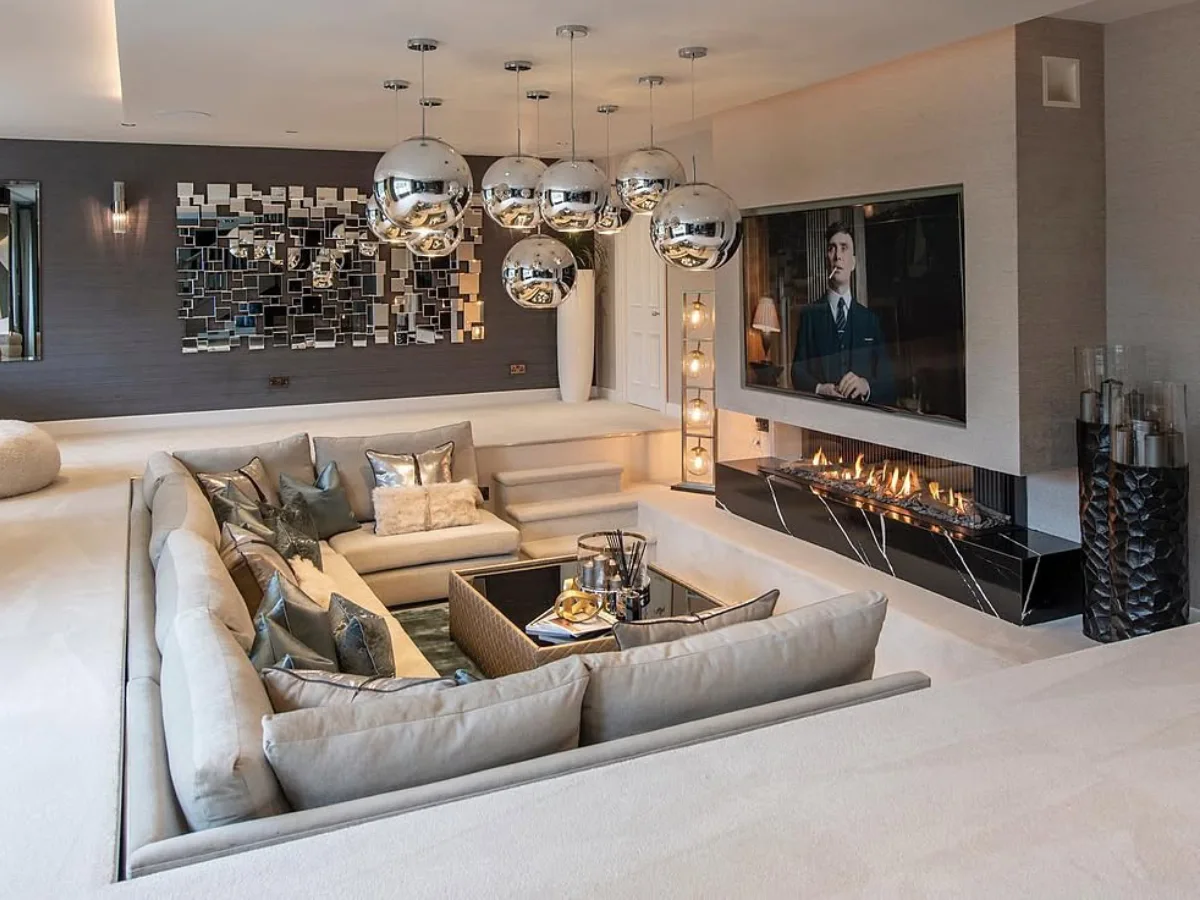 Luxurious sunken living room with a large sectional sofa, fireplace, TV wall, and modern pendant lights.