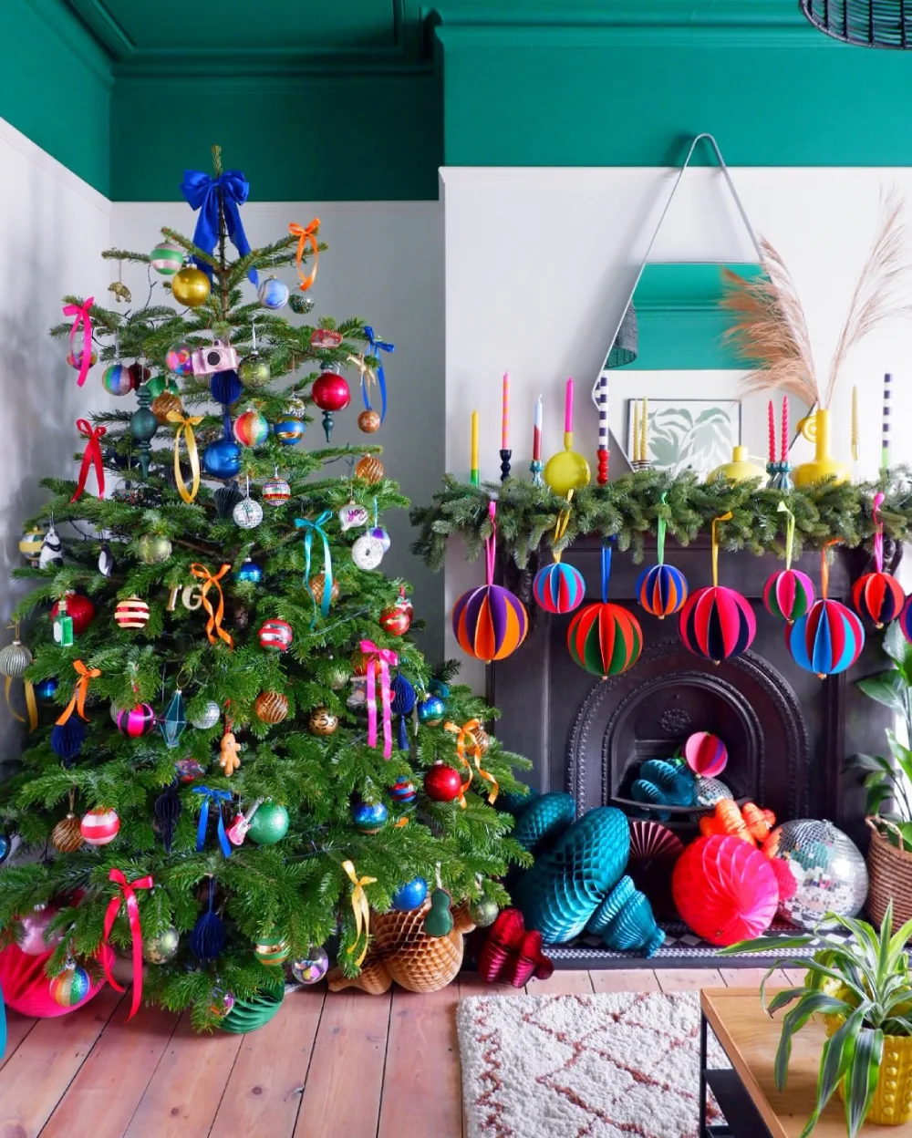 Colorful Christmas tree decorated with bright ornaments and ribbons beside a fireplace