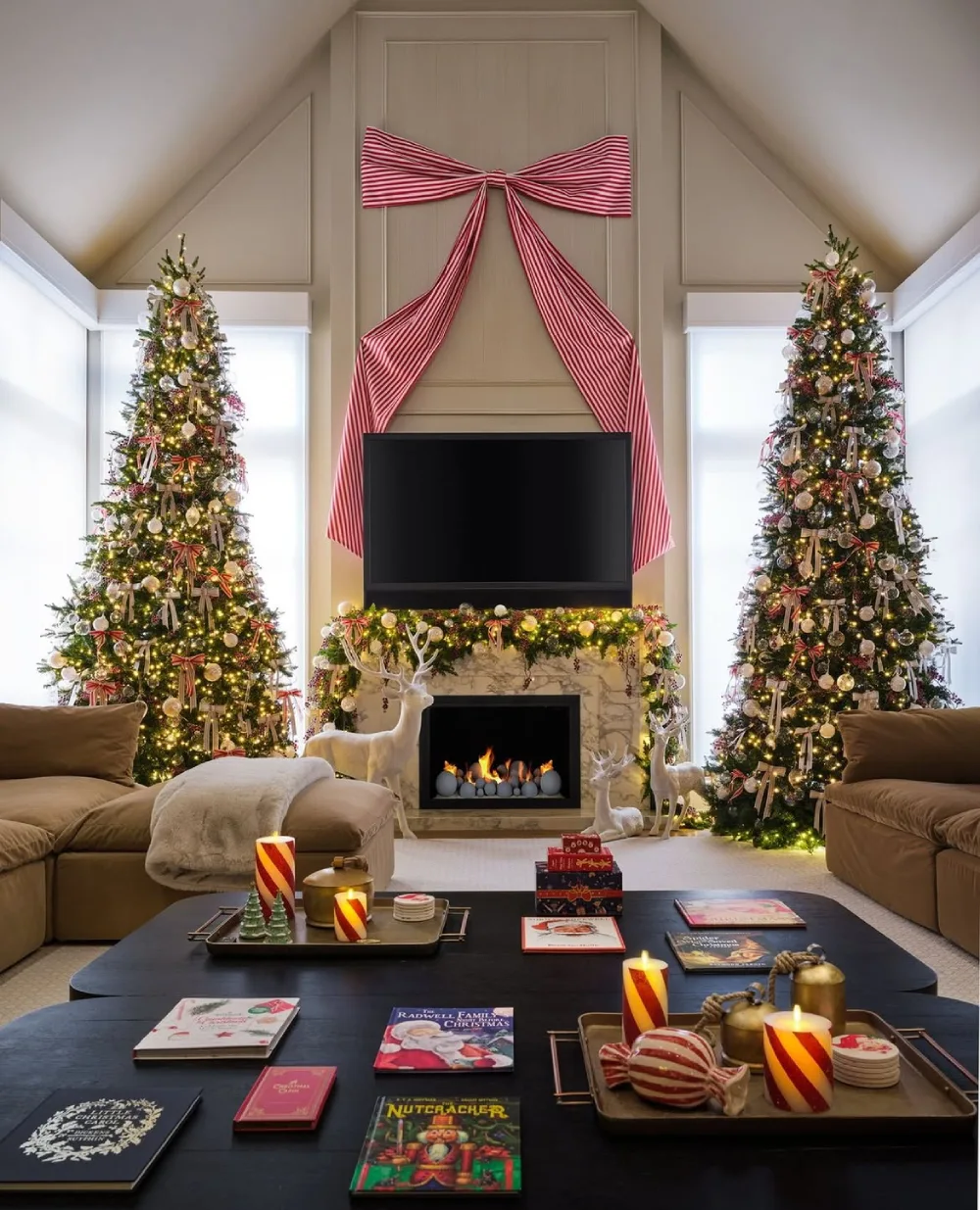 Living room with twin decorated Christmas trees, striped red bow, fireplace, and white reindeer