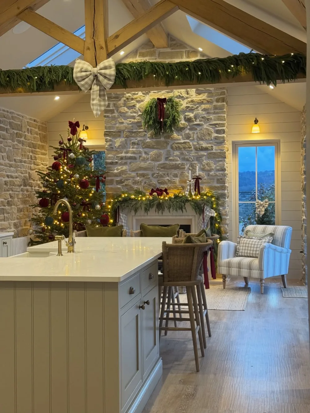 Rustic Christmas living room with exposed beams, stone fireplace, greenery, and a decorated tree