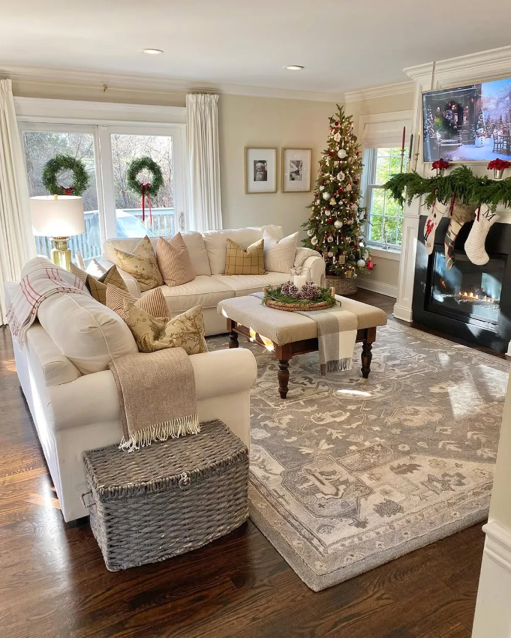 Light and cozy Christmas living room with white sofas, decorated tree, wreaths, and fireplace stockings