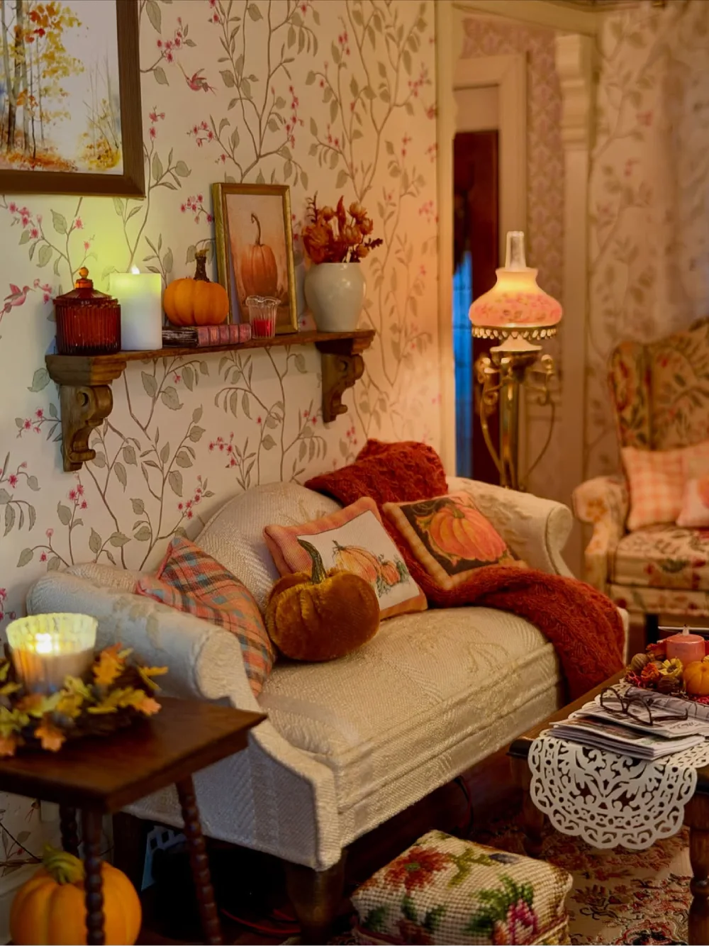 Vintage-inspired fall living room with floral wallpaper, a cream sofa, pumpkin-patterned pillows, rust-colored blankets, and antique-style table lamps