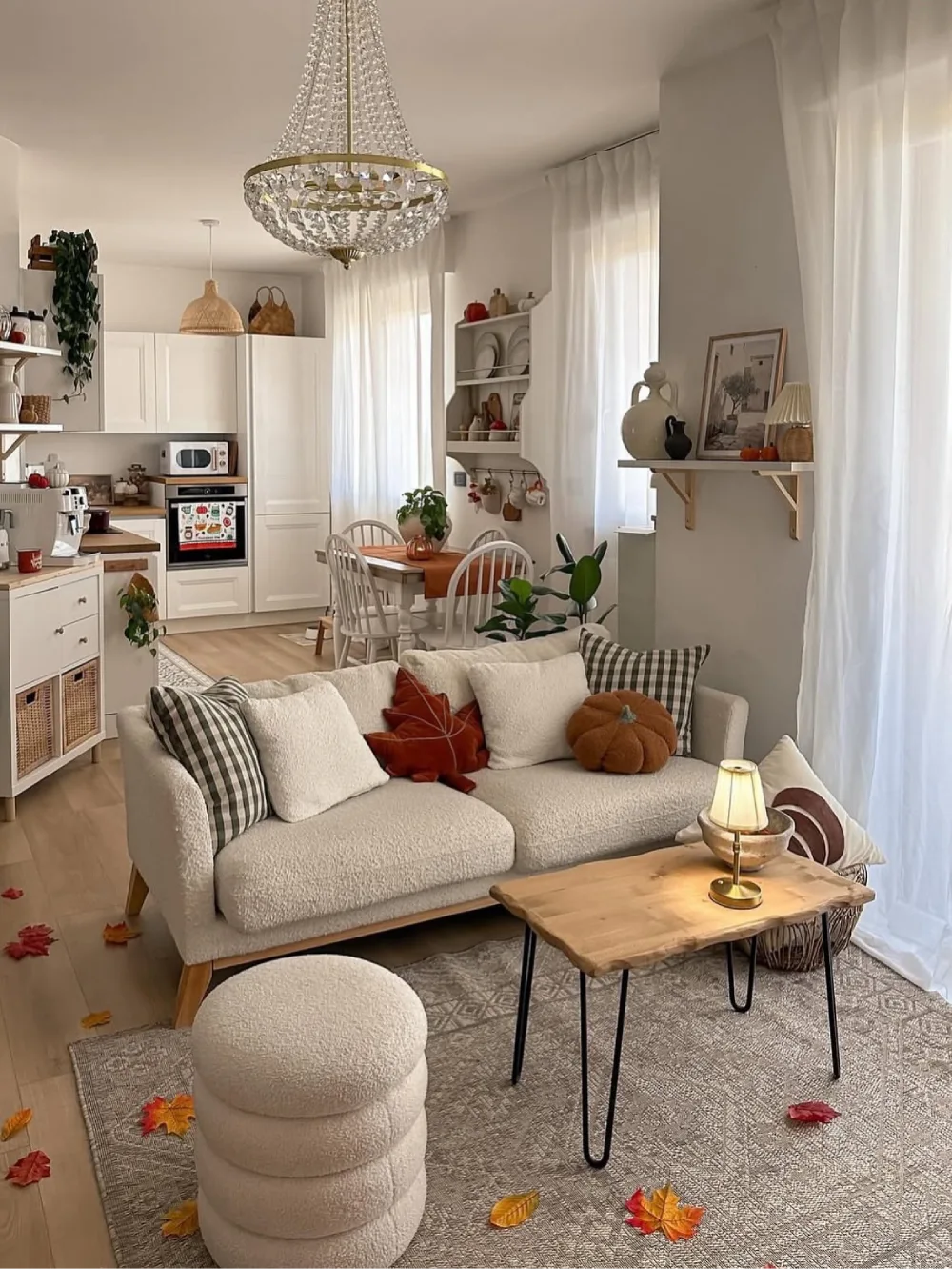 Minimalist neutral living room with a cream boucle sofa, rust and brown fall pillows, a pumpkin cushion, and scattered autumn leaves