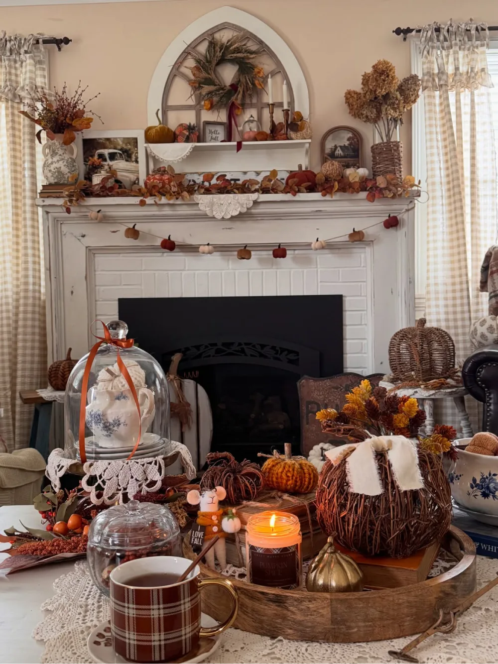 Rustic fall coffee table decorated with a wooden tray, miniature pumpkins, a glowing pumpkin spice candle, autumn florals, and vintage tableware