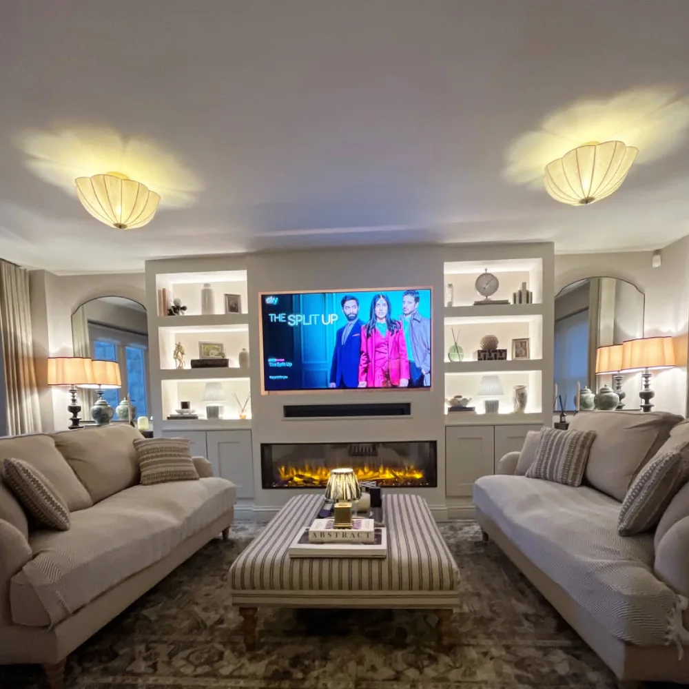 Contemporary living room with illuminated built-in shelves flanking a fireplace and wall-mounted television, featuring decorative vases, books, closed cabinets, and neutral sofas.