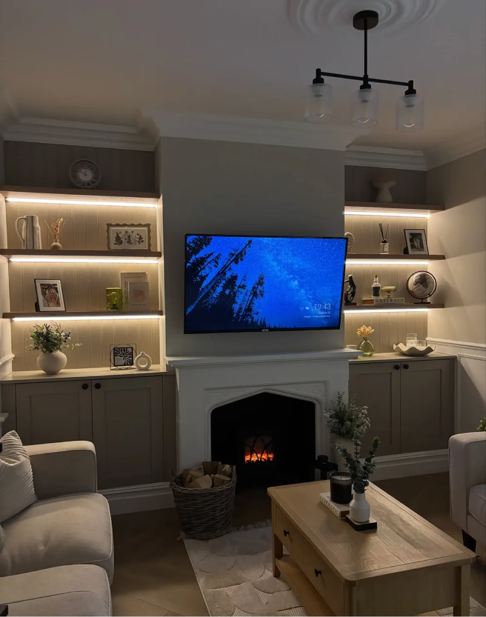 Living room fireplace with built-in floating shelves, subtle LED strip lighting, framed photographs, decorative vases, and dark lower cabinets.