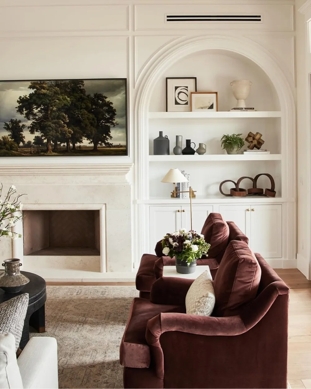 White arched built-in living room shelves beside a traditional fireplace, styled with neutral pottery, framed artwork, books, and decorative accessories.