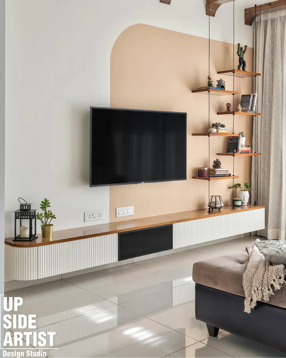 Modern living room TV wall with suspended wooden display shelves, a beige accent panel, decorative figurines, books, and a long white fluted media console