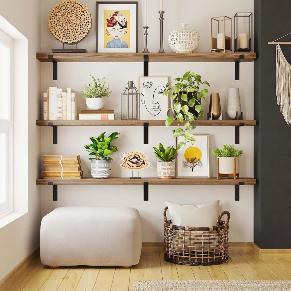 Three long walnut floating shelves with black metal brackets above a cream ottoman, styled with potted plants, framed artwork, books, and decorative vases
