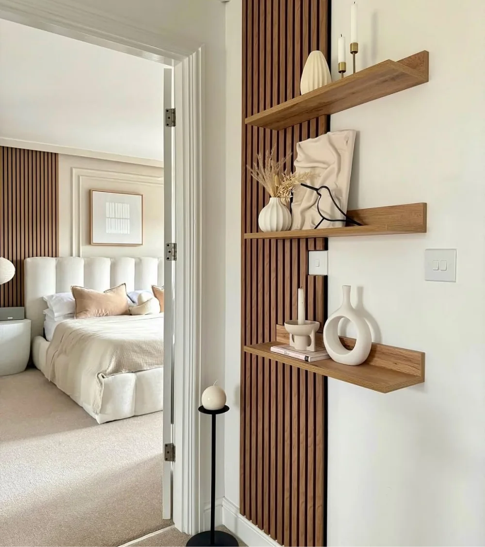 Modern walnut floating shelves mounted over vertical wood slat panels in a neutral living room, styled with sculptural ceramic vases, candles, and dried botanical stems