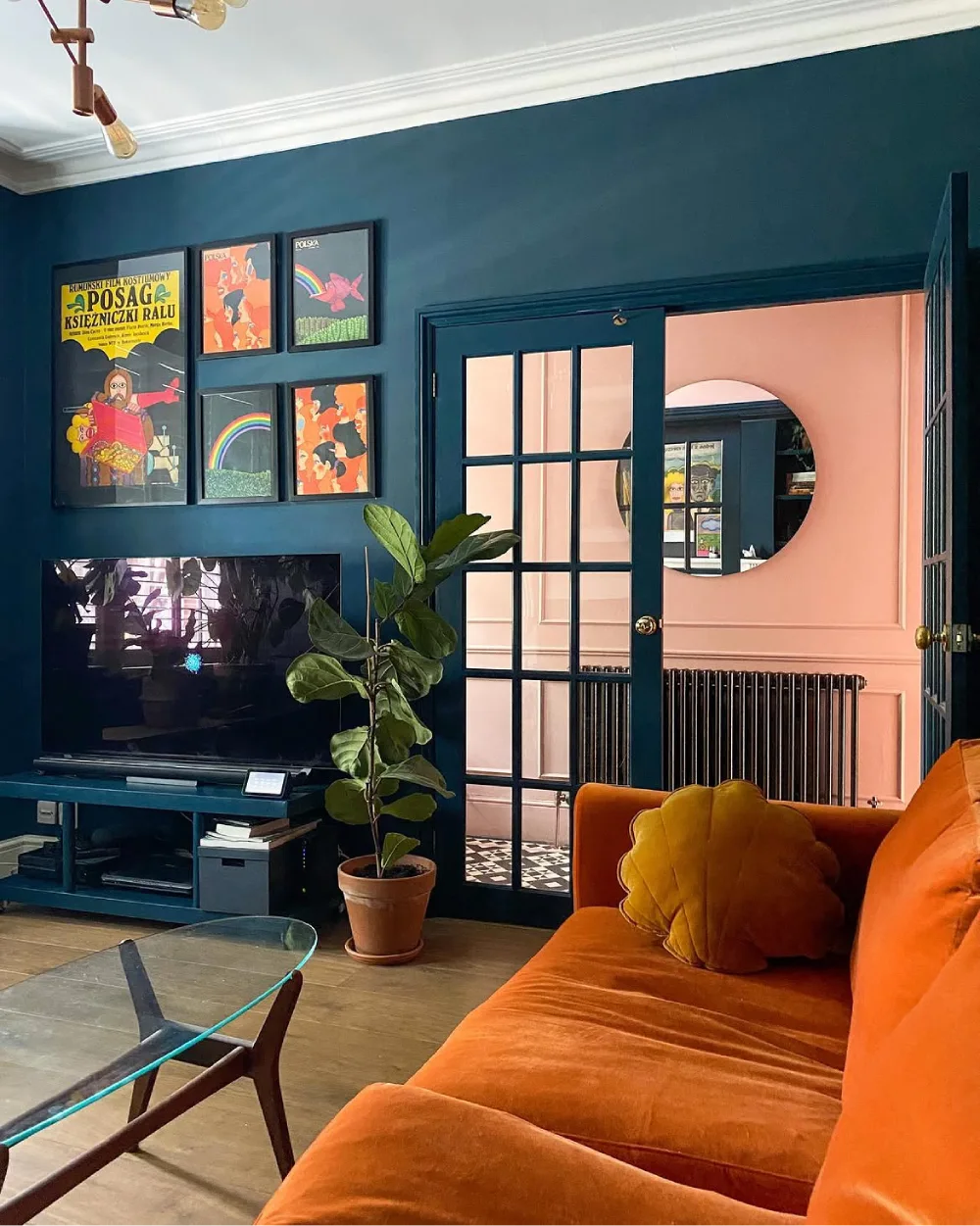 Moody living room with deep teal walls, an orange velvet sofa, colorful gallery wall, and peach accent wall