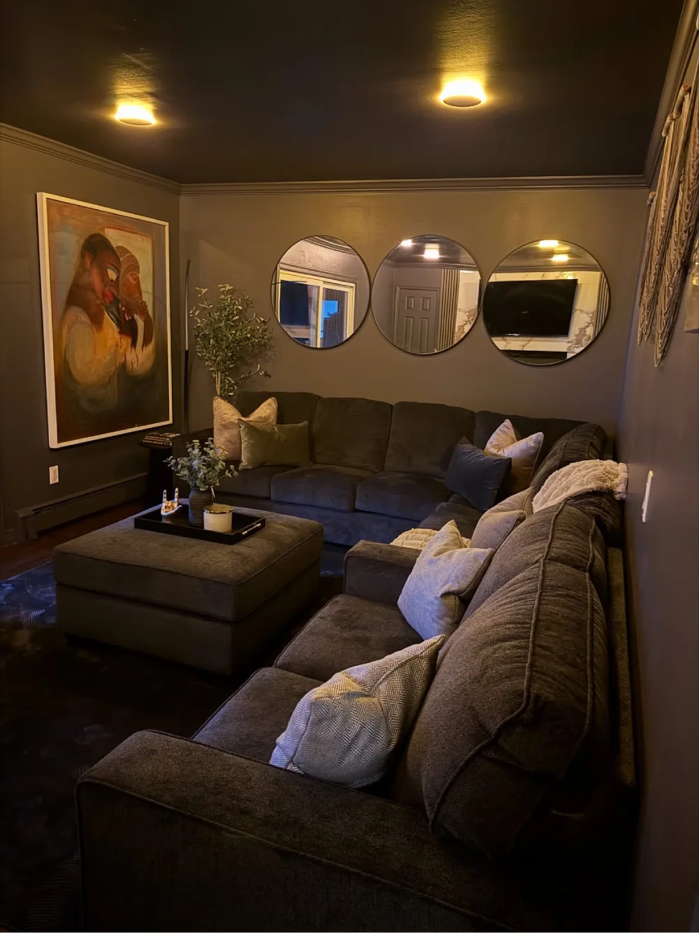 Cozy dark living room with charcoal walls, a deep gray sectional sofa, round mirrors, and warm ambient lighting