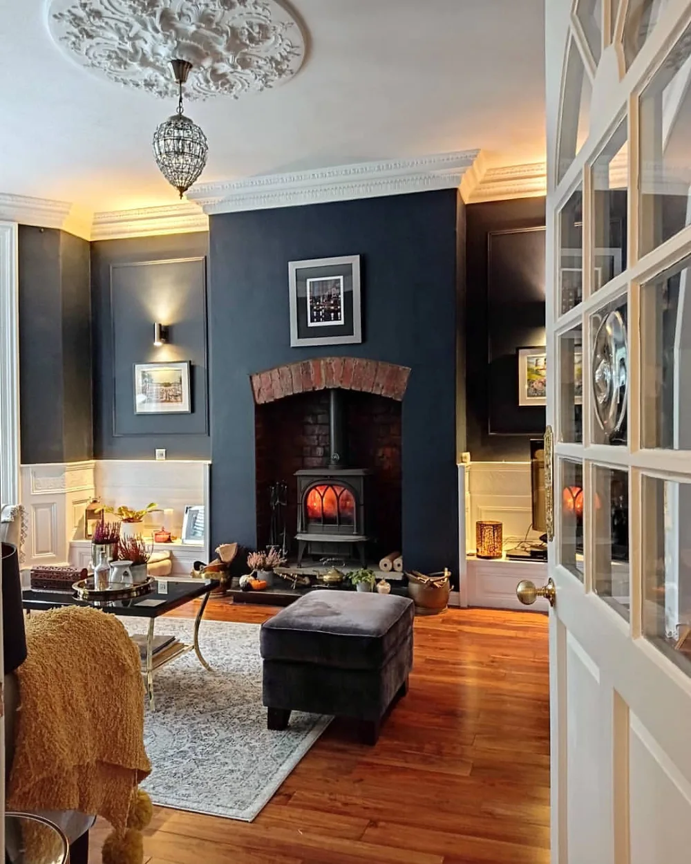 Traditional living room with navy walls, a brick fireplace, white wall paneling, and warm wood floors