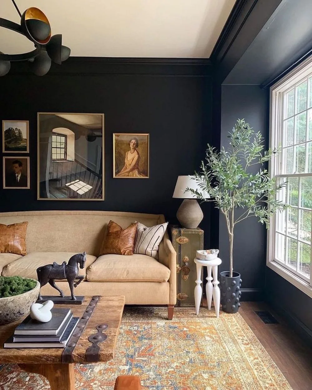 Moody living room with black walls, a cream sofa, warm wood coffee table, framed artwork, and large windows