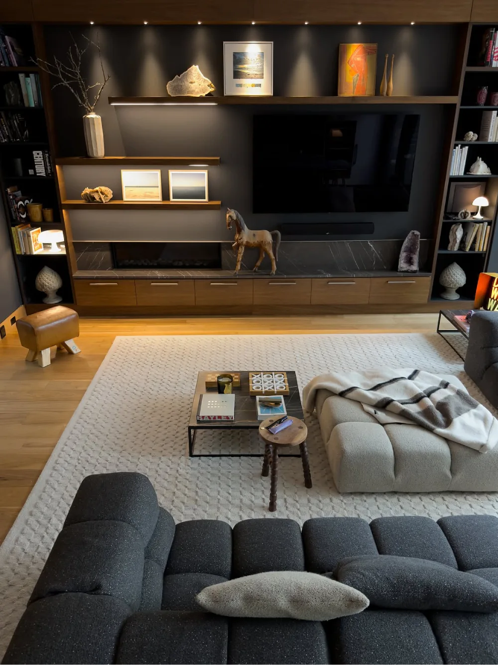 Modern moody living room with a charcoal media wall, built-in bookshelves, warm wood cabinetry, and a large television