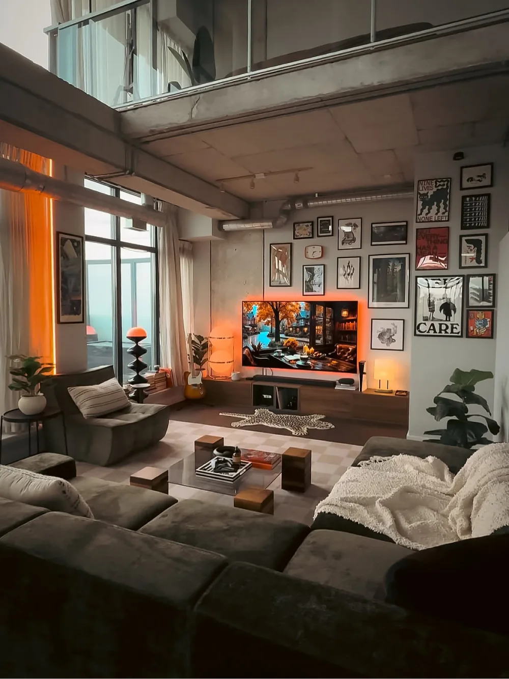 Industrial moody living room with a dark sectional sofa, exposed concrete ceiling, gallery wall, and warm orange accent lighting