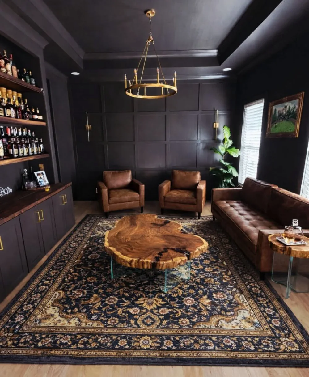Dark masculine lounge with black paneled walls, brown leather seating, built-in bottle shelves, and a rustic wood coffee table