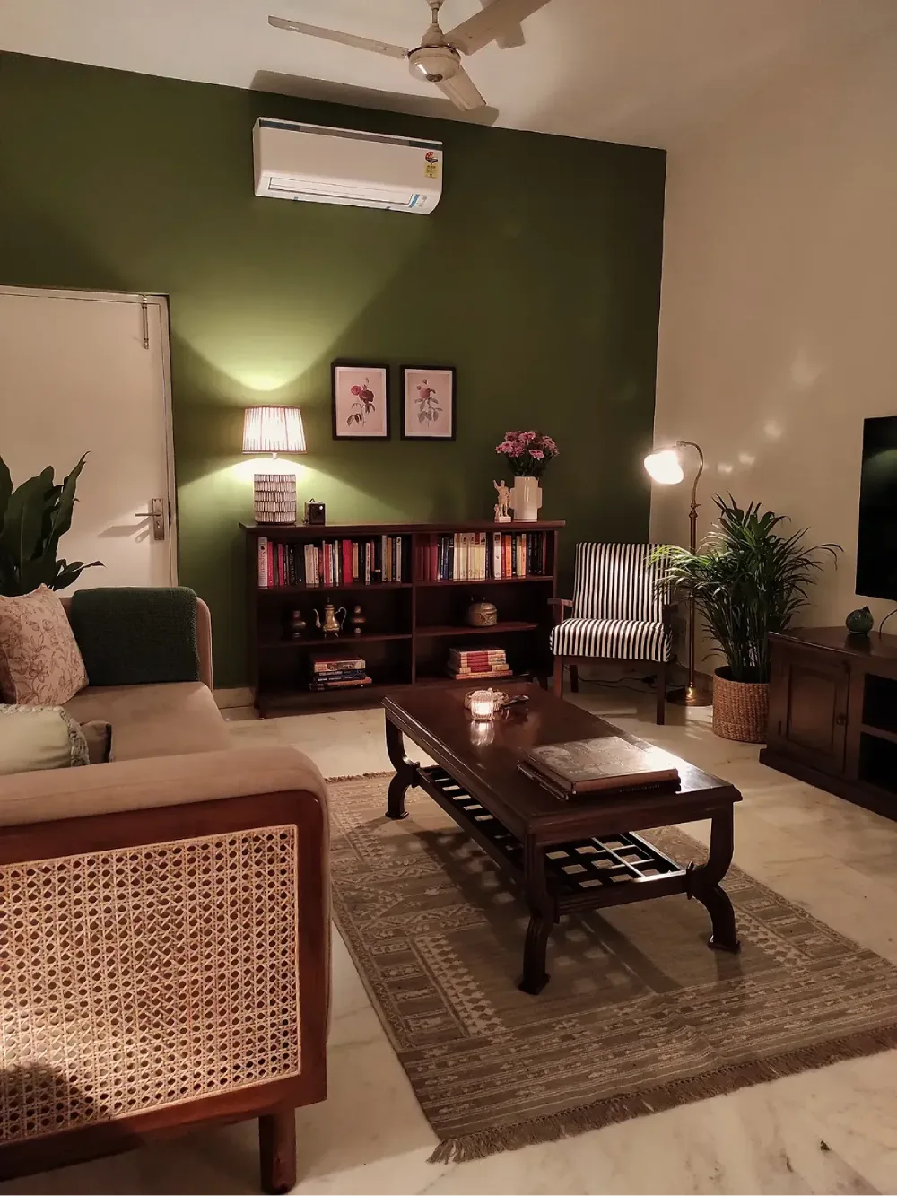 Cozy living room with a deep green accent wall, dark wood furniture, cane-backed seating, and warm ambient lighting