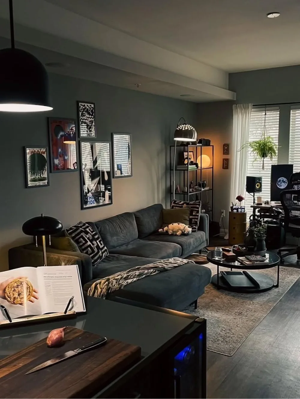 Modern moody living room with slate gray walls, a charcoal sectional, black pendant lighting, and abstract artwork