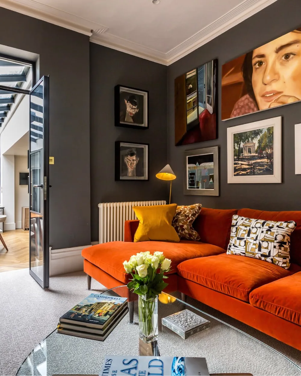 Moody living room with charcoal walls, a vibrant orange sectional sofa, mustard yellow pillows, and an eclectic gallery wall