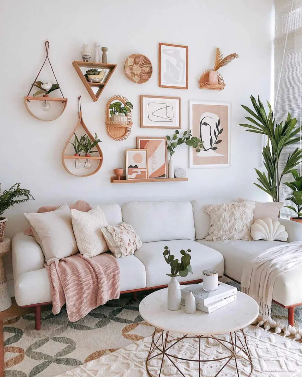 Soft boho living room with a white sofa, blush pink throws, textured cream pillows, botanical decor, a patterned rug, and natural wood accents.
