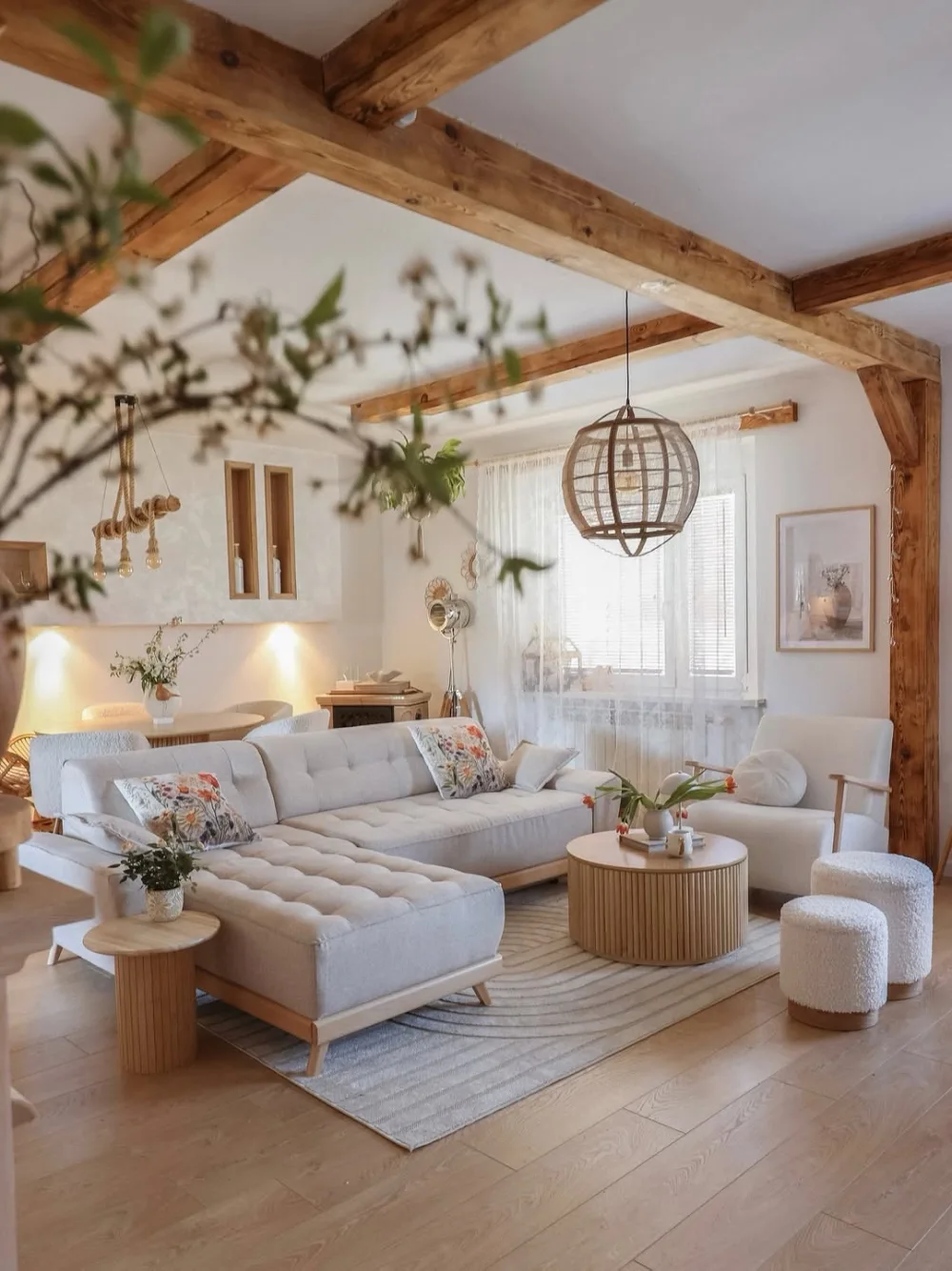 Farmhouse living room with exposed wooden ceiling beams, a light gray sectional sofa, natural wood furniture, and a woven pendant light