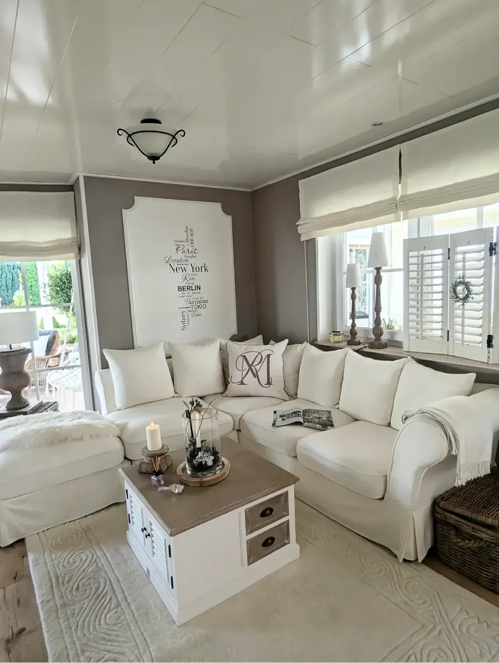 Cozy farmhouse living room with a white sectional sofa, taupe walls, rustic coffee table, textured cream rug, and woven storage basket