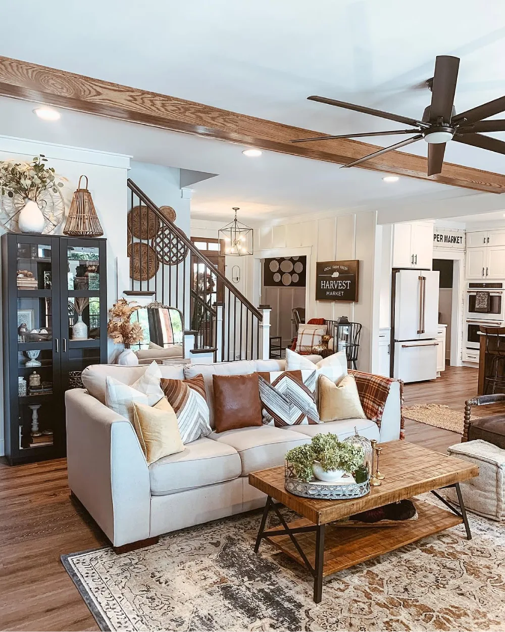 Farmhouse living room with a white sofa, leather and plaid pillows, rustic wooden coffee table, vintage rug, and exposed ceiling beam