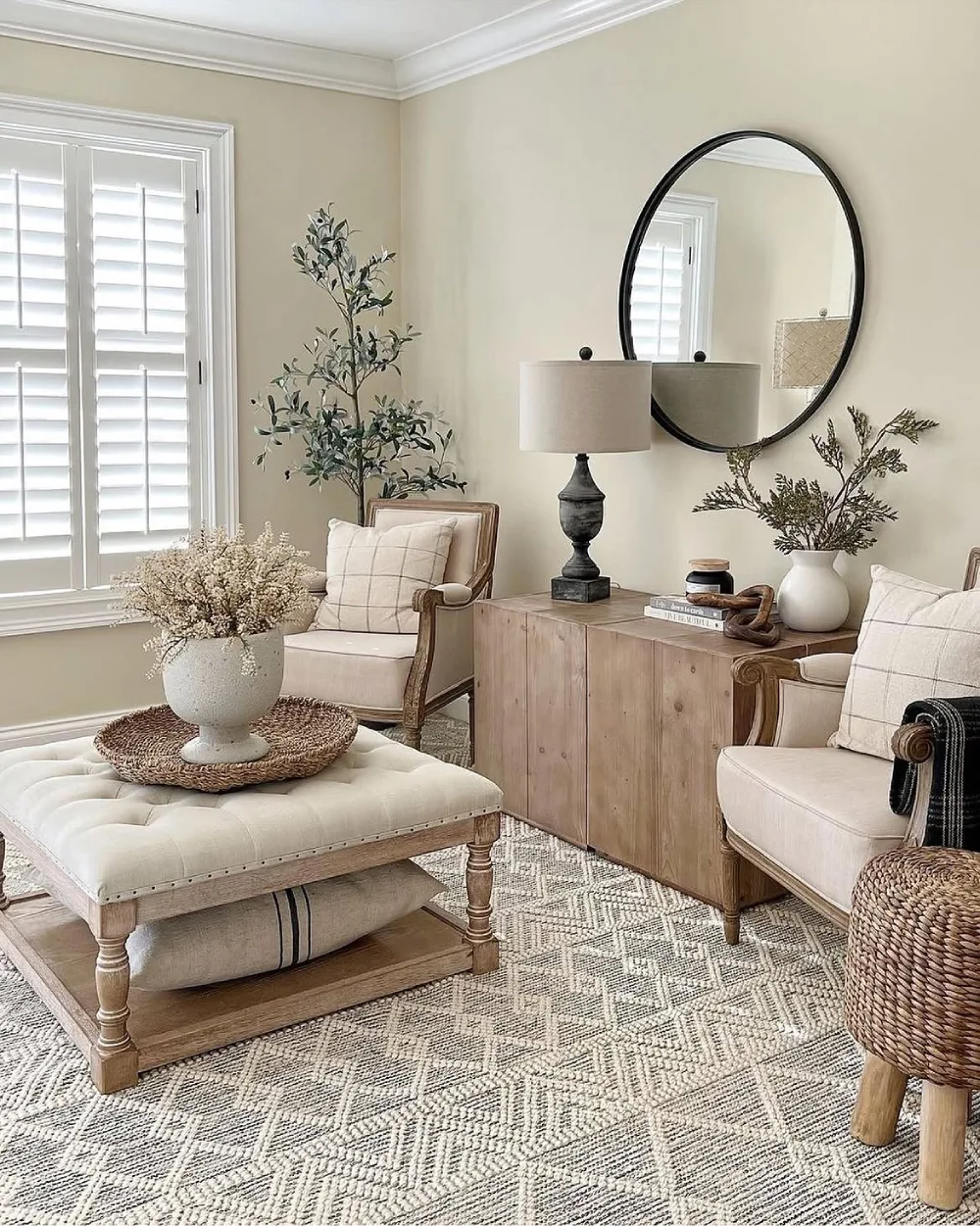 Neutral farmhouse sitting area with natural wood furniture, cream upholstered chairs, a woven rug, and simple botanical decor