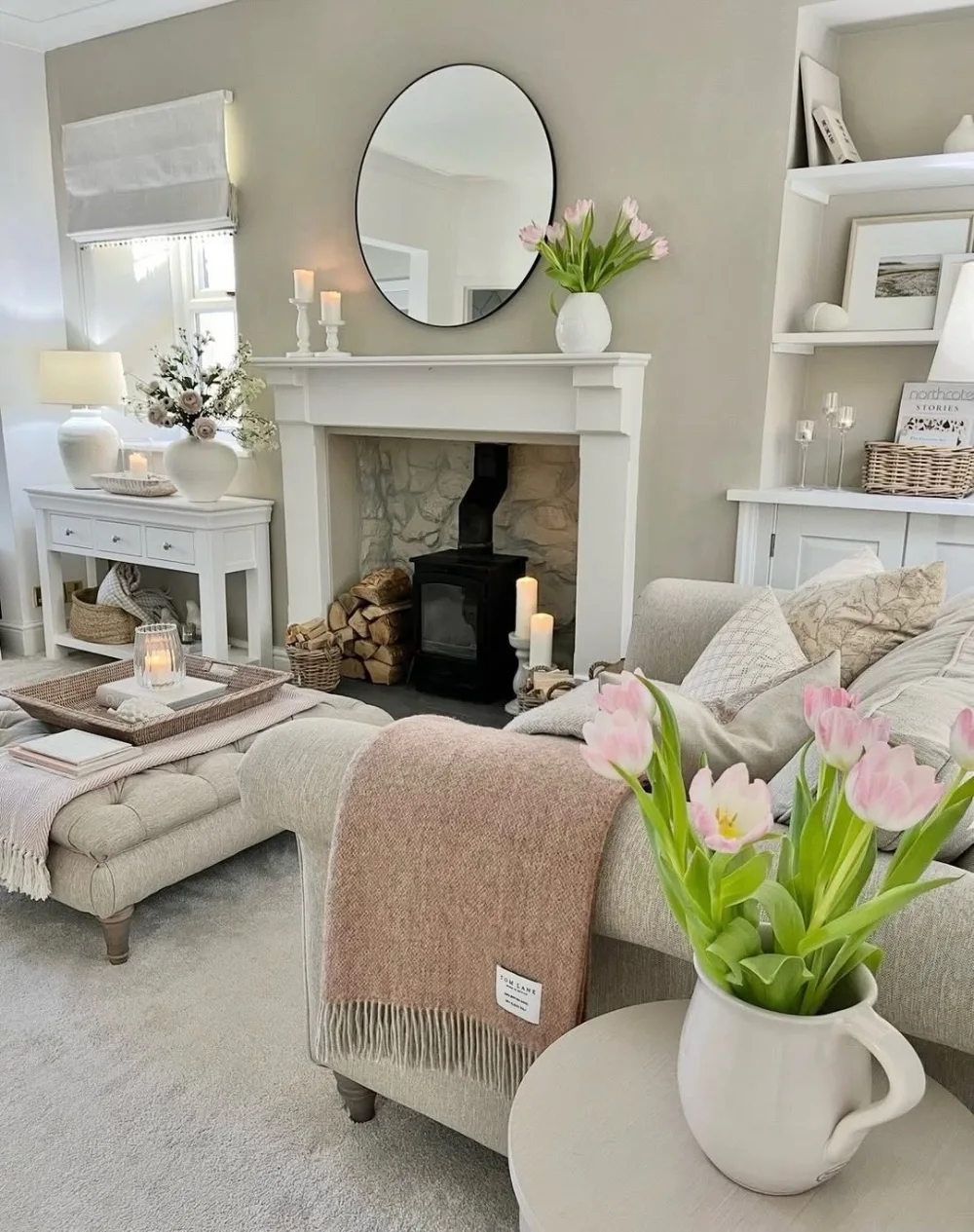 Cozy farmhouse living room with a cream sectional, blush pink throw, pink tulips, white fireplace, and neutral decorative pillows