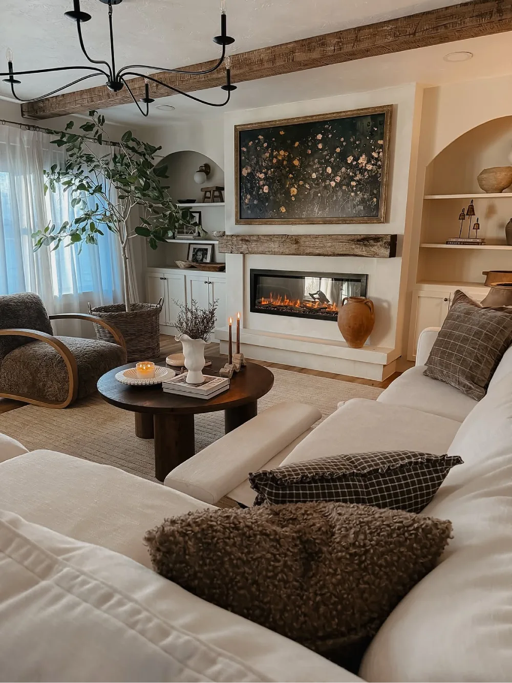 Cozy farmhouse living room with a white fireplace, rustic wood mantel, dark coffee table, textured neutral pillows, and a chunky knit throw