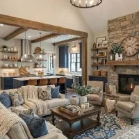 Farmhouse living room with a beige sofa, blue accent pillows, a rustic wooden coffee table, exposed ceiling beams, and a stone fireplace.