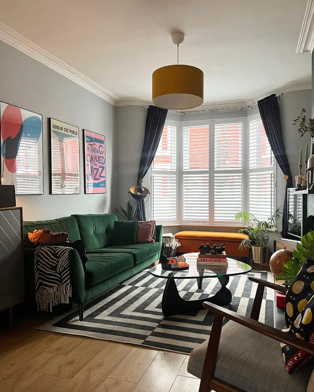Small living room with a deep green sofa, geometric rug, bay window, and colorful artwork