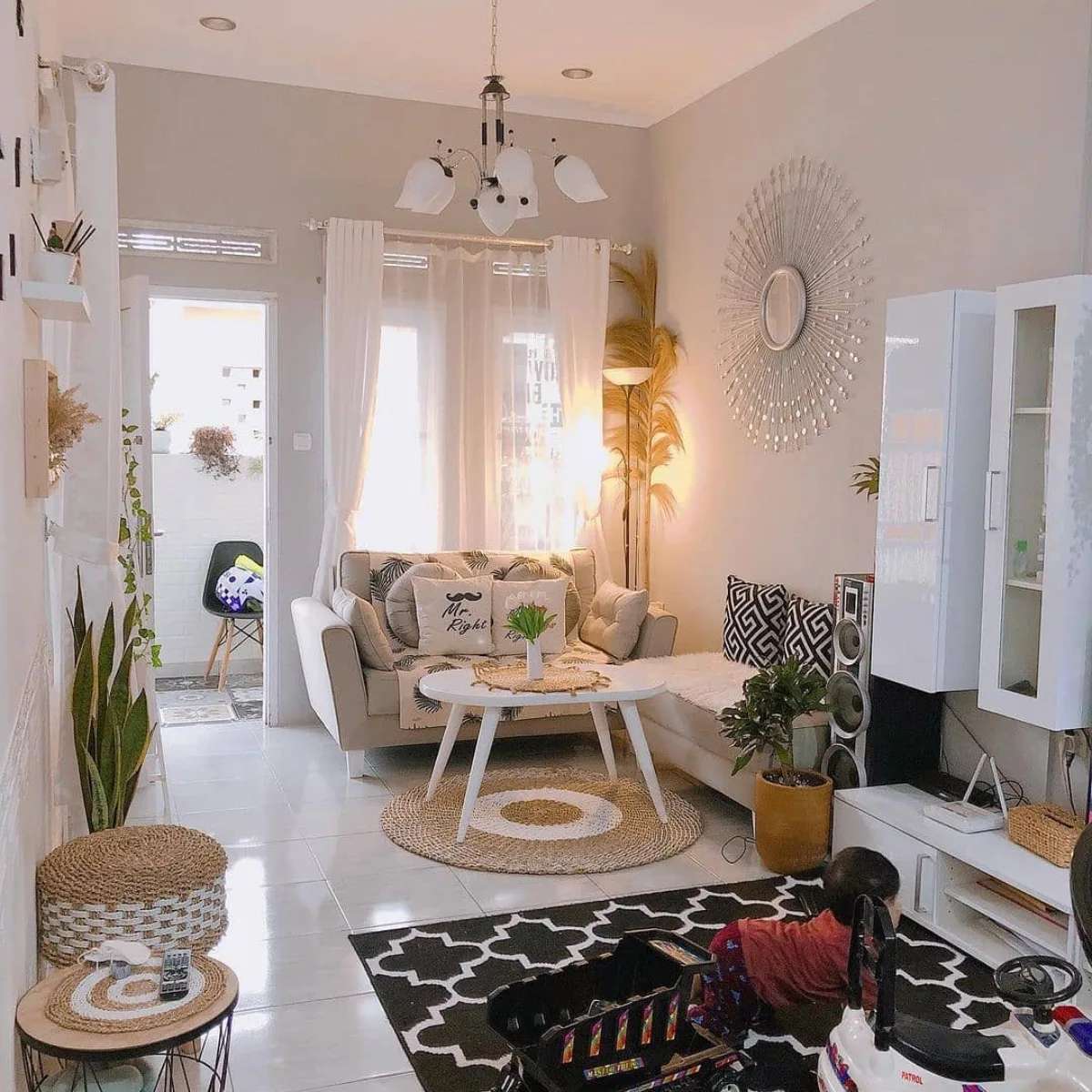Cozy small living room with a neutral sofa, layered rugs, plants, and decorative wall mirror